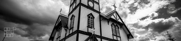 Black and white view of a wooden church beneath layered clouds.