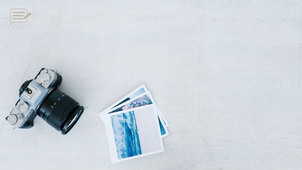 A camera and a small stack of photographic prints on a pale surface.