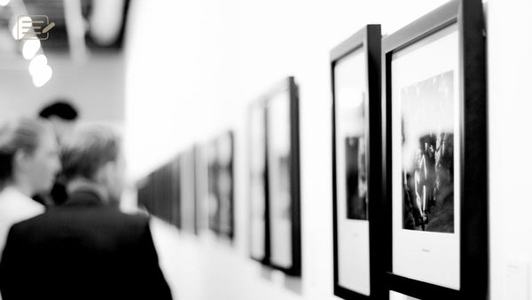 Visitors viewing framed black and white photographs along a gallery wall.