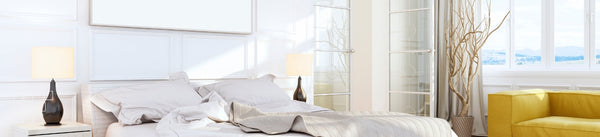 Bedroom wall art above a white bed with lamps and yellow seating