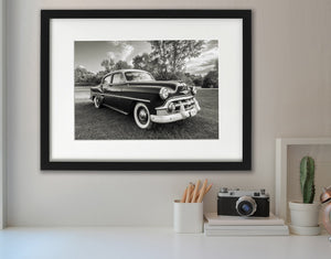 1953 Chevrolet sedan beneath trees and a lightly clouded Route 66 sky