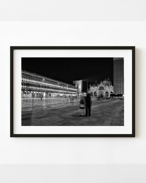 Blurred couple in illuminated St Mark’s Square Venice at night in black and white