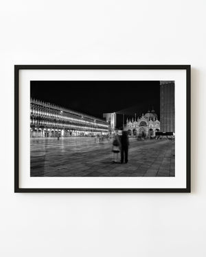 Blurred couple in illuminated St Mark’s Square Venice at night in black and white