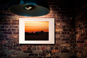 A pale farmhouse roof sits among dark trees beneath orange dawn clouds.