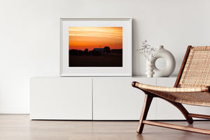 A quiet farmhouse roofline against an expansive orange morning sky.