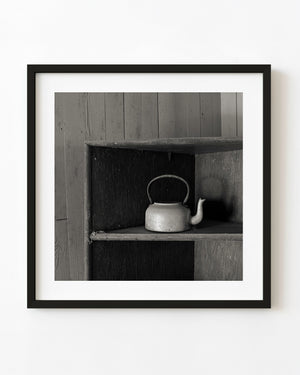 A teapot left on a wooden shelf in an abandoned Clarence Town home, photographed in black and white.