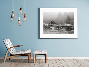 Exposed timber and raised walkways beside water below fog-softened conifers.