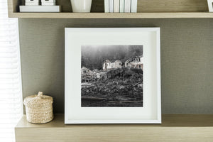 Monochrome British Columbia shoreline with abandoned buildings and long fallen timbers.