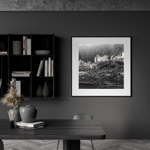 Black and white coastal ruins with rough wood, overgrown slopes and forest behind.