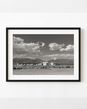 Abandoned California school near Route 66 beneath desert mountains and scattered clouds.