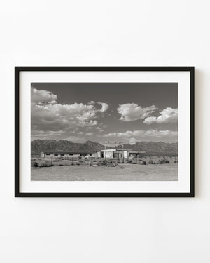 Abandoned California school near Route 66 beneath desert mountains and scattered clouds.