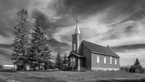 Boarded church windows and a steeple beneath a dramatic Saskatchewan sky.