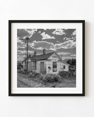 Abandoned Currie railway station beneath bright clouds, photographed in black and white.