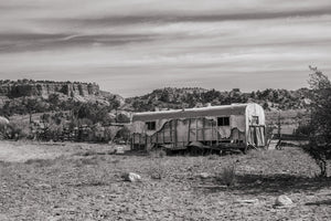 Weathered trailer with buckled siding and dark windows in an open desert landscape.