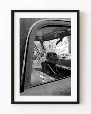 Abandoned Dodge truck interior with a steering wheel and weathered dashboard in black and white.