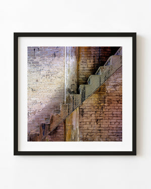 Diagonal factory stairs against a weathered brick wall with peeling paint.