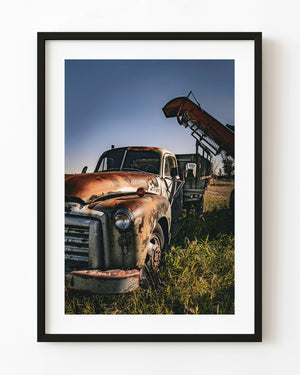 Rusted GMC farm truck beneath raised machinery and a blue sky in southern Alberta.
