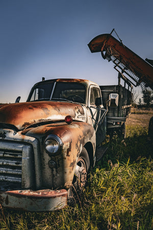 Colour photograph of an abandoned GMC truck surrounded by tall prairie grass.
