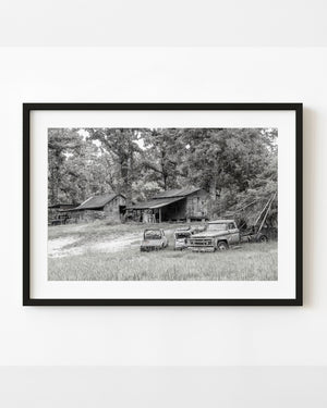 Abandoned GMC tow truck and weathered wooden sheds in the American South, photographed in black and white.