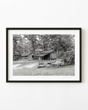 Abandoned GMC tow truck and weathered wooden sheds in the American South, photographed in black and white.