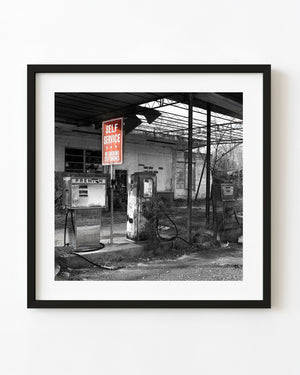 Abandoned Georgia gas pumps beneath a red SELF SERVICE sign in a mostly monochrome photograph.