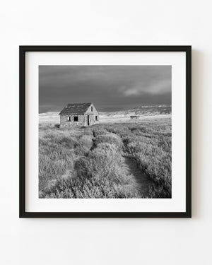 Abandoned Southwest house at the end of a track beneath a heavy sky, photographed in black and white.