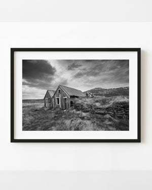 Abandoned Icelandic turf farmhouse with wooden gables and grass-covered stone walls in black and white.