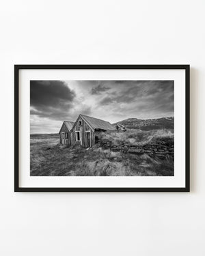 Abandoned Icelandic turf farmhouse with wooden gables and grass-covered stone walls in black and white.