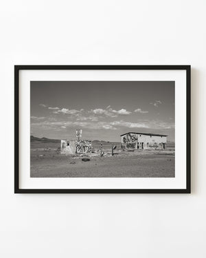 Abandoned Nevada motel covered in graffiti beneath a cloud-filled sky, black and white