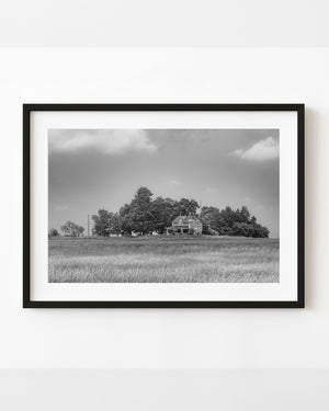 Abandoned Ontario farmhouse across a grassy field beneath a broad sky, black and white