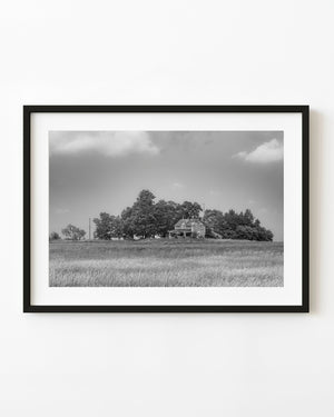 Abandoned Ontario farmhouse across a grassy field beneath a broad sky, black and white
