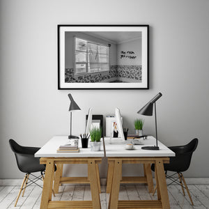 Black and white photograph of graffiti on a pale wall above floral wallpaper