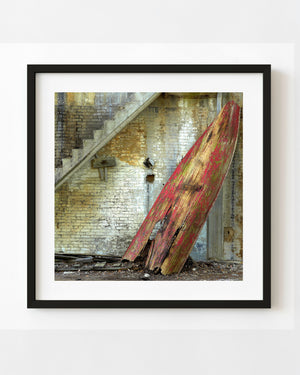 Abandoned red wooden rowboat leaning against a weathered brick wall beneath concrete stairs