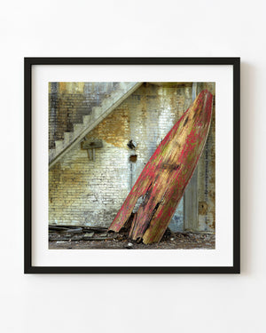 Abandoned red wooden rowboat leaning against a weathered brick wall beneath concrete stairs