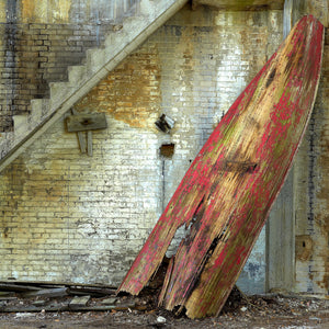 Peeling red paint exposes bare wood on a rowboat inside an abandoned Ontario factory
