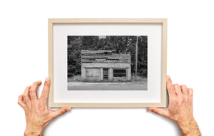 Boarded and open windows flank a narrow door beneath broken wooden siding