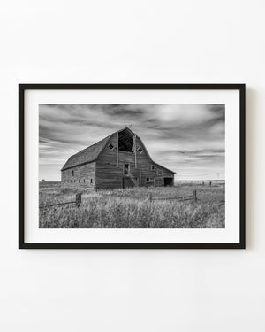 Abandoned Saskatchewan barn with an open loft beneath layered clouds, black and white