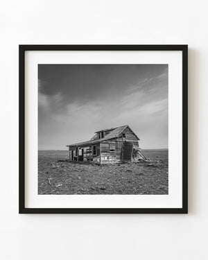Abandoned Saskatchewan farmhouse beneath a wide streaked sky in black and white