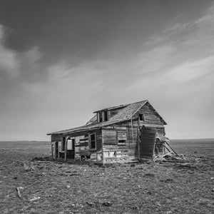 Broken wooden siding and dark window openings on an isolated prairie house