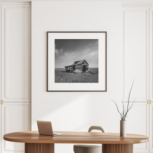 A weathered farmhouse stands in an open Saskatchewan field with a collapsed side section