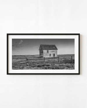 Abandoned Saskatchewan farmhouse beyond a rail fence in black and white