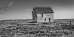 A weathered prairie house stands in open grassland beneath a broad sky