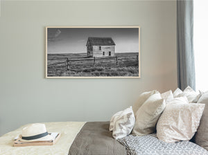 An isolated farmhouse rises above rolling prairie grass and a low rail fence