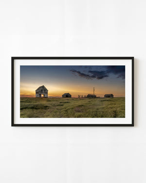 Abandoned Saskatchewan farmhouse beneath a blue sky and golden sunset.