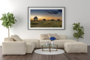 Golden sunset behind an old farmhouse and low outbuildings on the prairie.