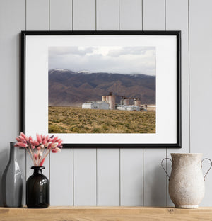 An abandoned industrial plant sits low against mountain slopes with patches of snow.