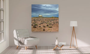 Scattered desert plants surround an abandoned schoolhouse beneath a broad cloudy sky.