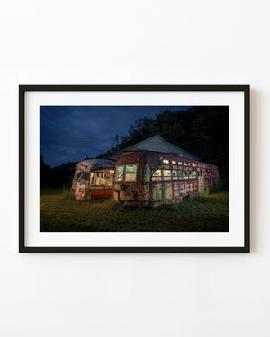 Two abandoned trolley cars beneath a deep blue sky with warm light in their windows.
