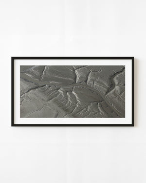 Branching coastal channels and fine ridges across grey ground in an aerial view of Alaska.