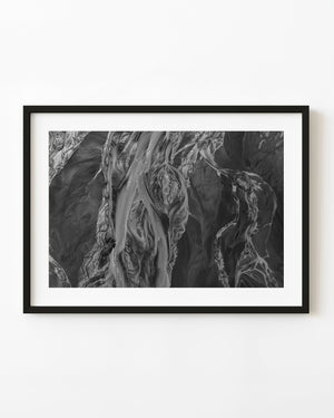 Braided river channels crossing dark coastal sediment in an aerial photograph of Alaska.